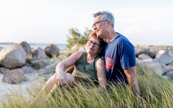 A happy couple sitting in the grass on the beach smiling together | Icon Cancer Centre